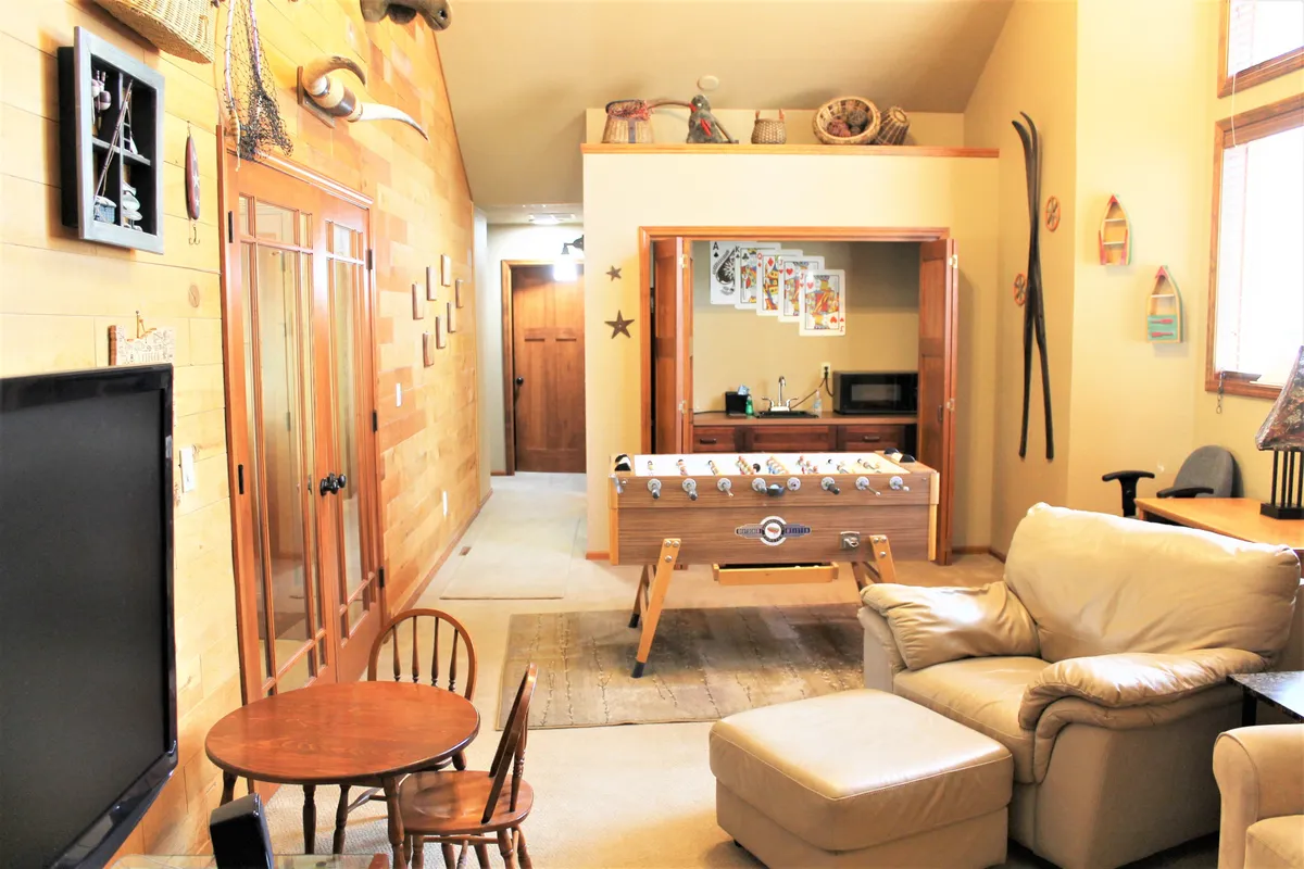 This image features a foosball table as the clear focal point, alongside a small dining table, comfortable armchair, and decorative wall art. The setting is casual and inviting, suggesting a lively, multi-use space ideal for socializing, playing games, and relaxing.