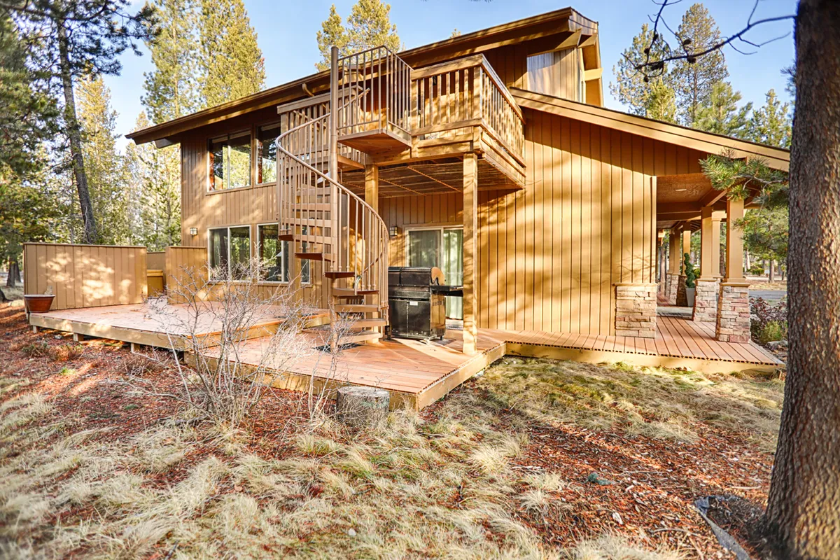 This exterior shot highlights the deck area, featuring a grill, ample space for outdoor dining, and a distinctive spiral staircase leading to another level. The large windows hint at the connection between indoor and outdoor spaces. The scene suggests opportunities for barbecues, family meals, and lounging in the sunshine.