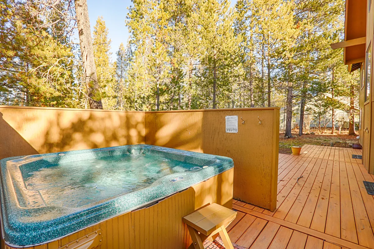 This image captures a tranquil view of the wooden wrap-around deck with a bubbling hot tub in the foreground, surrounded by tall trees that embody the natural beauty of Sunriver. The deck looks spacious, perfect for both relaxation and socializing. The hot tub is situated to take advantage of the serene setting, ideal for stargazing or soaking after outdoor adventures.