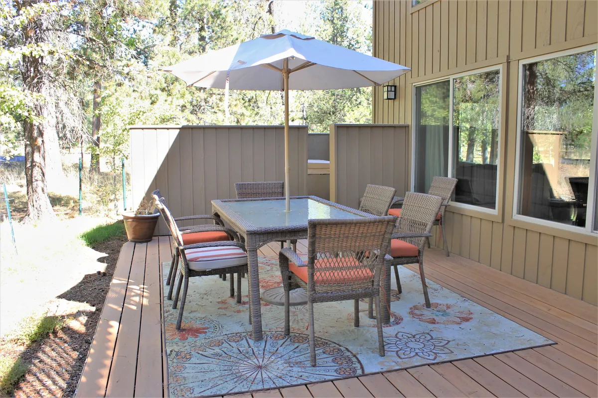 A cozy outdoor dining table with umbrella, surrounded by greenery and a decorative rug. The relaxed setup suggests a spot for family meals, sharing stories, or unwinding after a day of local exploration. The scene feels casual yet welcoming, with enough room for all ages to gather.