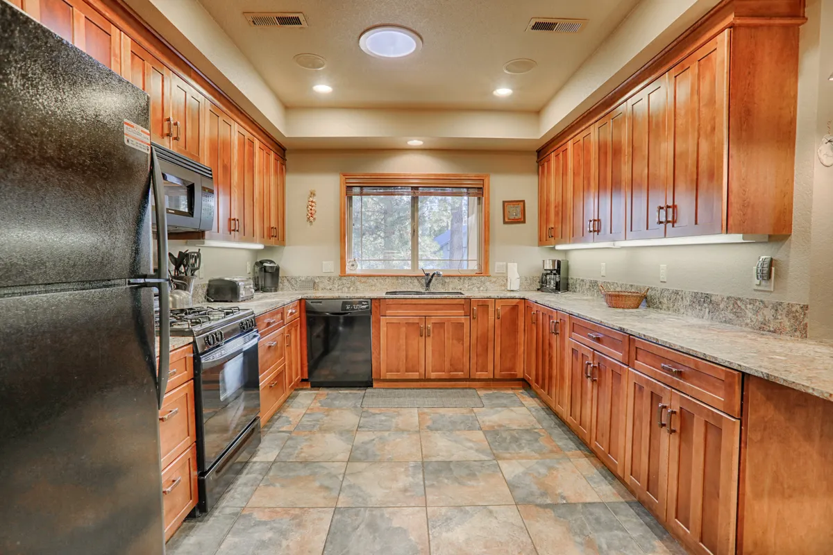 A kitchen filled with natural light, featuring a central island, wood cabinetry, and modern stainless steel appliances. The space is open and inviting, ideal for preparing big meals and socializing with guests or family.