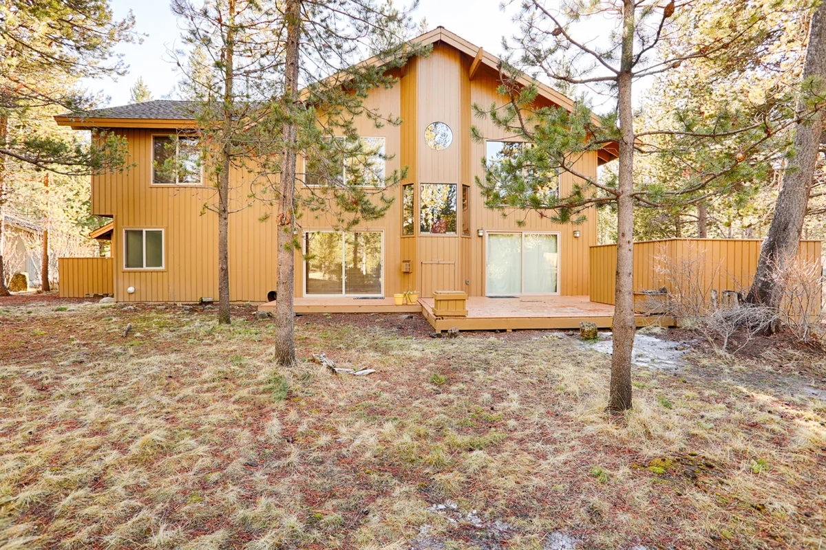 A peaceful view of the home’s large wooden deck nestled among tall pine trees, with ample space for outdoor gatherings and relaxation. The deck wraps around the house, framed by large windows and surrounded by natural beauty, inviting guests to soak up the outdoors in every season.