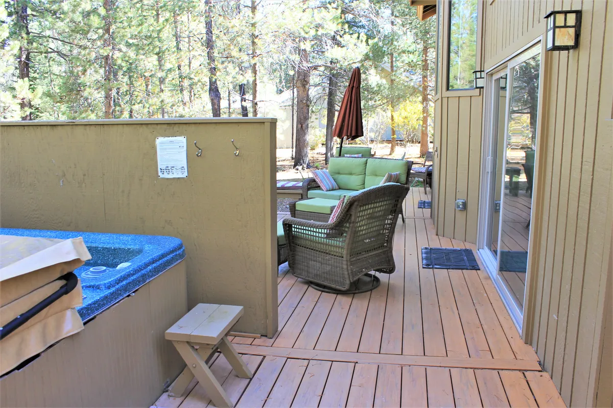 A wide view of the wooden deck featuring a hot tub, a comfortable seating area under an umbrella, and plenty of room for relaxing or entertaining. The setting is calm and inviting, making it ideal for enjoying coffee, reading, or socializing after a day of adventure. The presence of both the hot tub and deck seating provides a sense of variety for outdoor enjoyment.