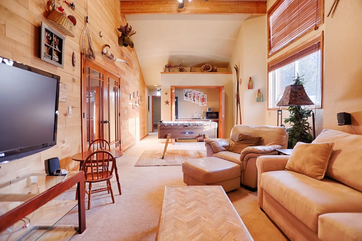 A cozy living area with a large TV, wooden walls, a comfortable sofa, decorative items, and a pool table. The space feels welcoming and is set up for both relaxation and entertainment, from movie nights to social gatherings.