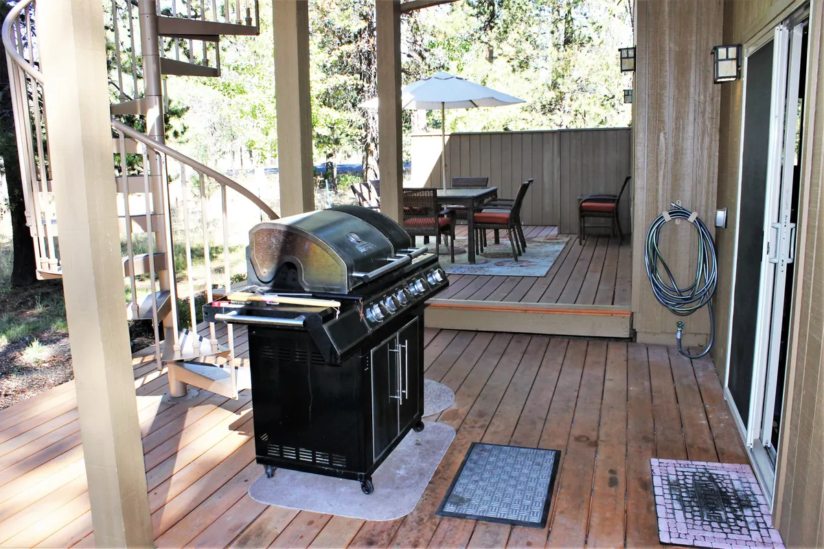 An outdoor scene featuring a grill, dining set, and a distinctive spiral staircase leading to an upper level. The setting is casual and ideal for barbecuing, socializing, or enjoying the outdoors, with seating for group activities.